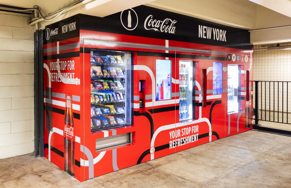 Side view of a Coca-Cola-branded automated retail enclosure with snack and beverage machines at the Second Avenue-East Houston subway station